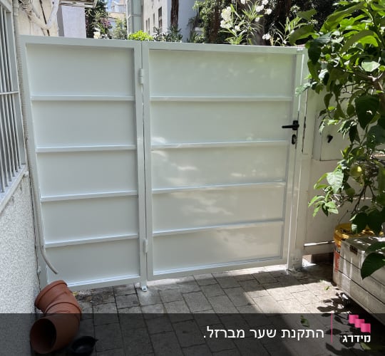 שער מתכת לבן עם ידית שחורה בגינה